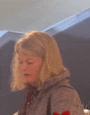 a woman with blonde hair is wearing a gray jacket and a red shirt .