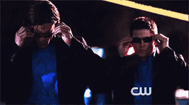 a man wearing sunglasses and a blue shirt is standing next to a man wearing sunglasses and a cw logo