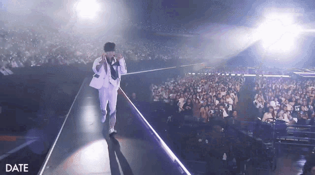 a man in a white suit stands on a stage in front of a crowd and the word date is on the bottom right