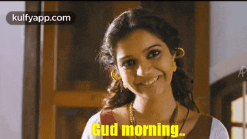 a woman is smiling and saying `` good morning '' while standing in front of a door .