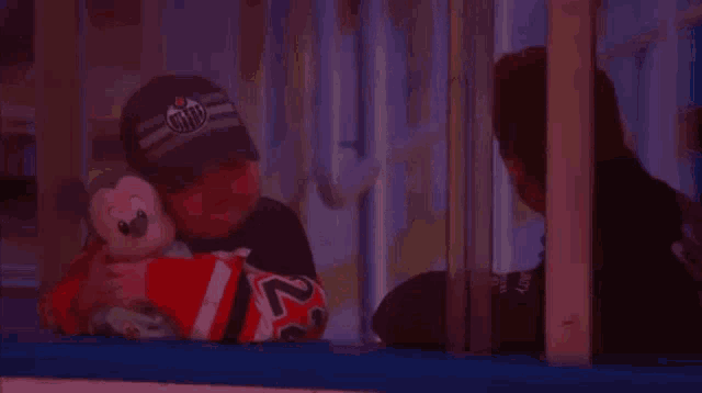 a man in an edmonton hat holds a stuffed animal