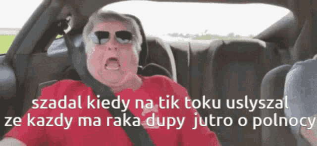 a man wearing sunglasses and a red shirt is driving a car with a foreign language caption