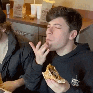 a man is eating a hamburger with a bag of chips in the background .