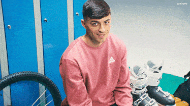 a man in a pink adidas sweatshirt sits next to a pair of ski boots .