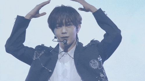 a young man wearing a black jacket and white shirt is making a heart with his hands
