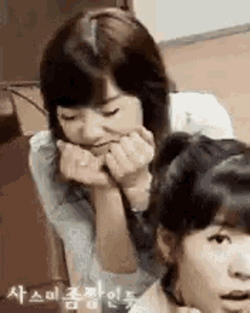 two girls are sitting next to each other with their hands on their chins .