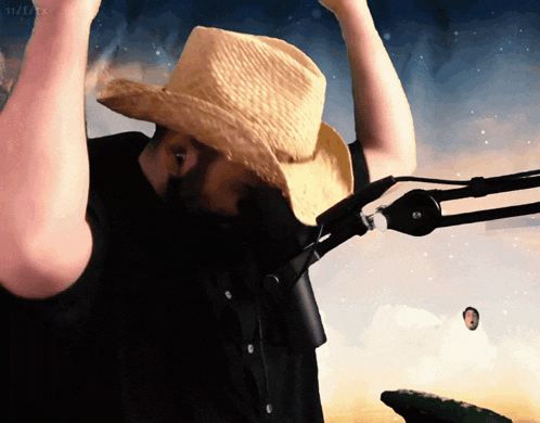 a man wearing a cowboy hat is standing in front of a microphone with his hands in the air