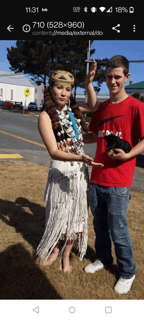 a man in a red nike shirt holds a small dog next to a woman in a native american dress