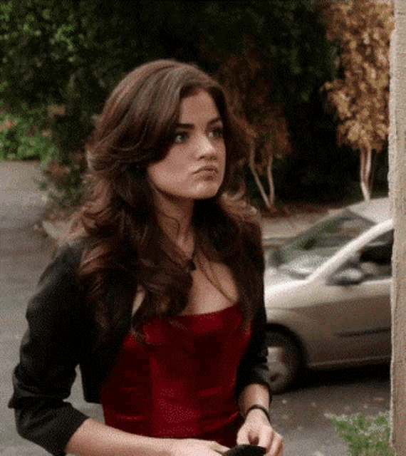 a woman in a red dress and black jacket is standing in front of a white car