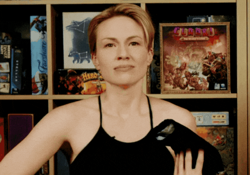 a woman stands in front of a shelf full of board games including a box of gumball