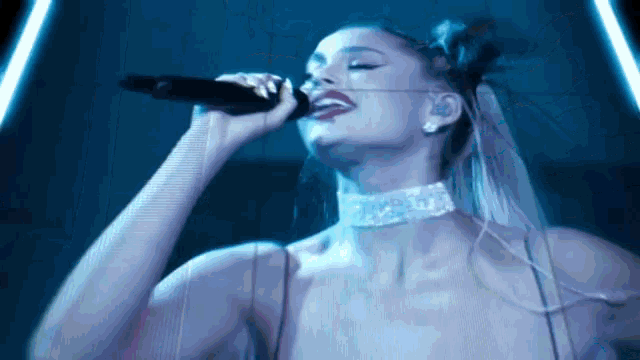 a woman singing into a microphone with a choker on her neck