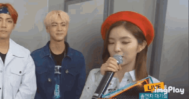 a girl in a red hat is holding a microphone in front of a sign that says live