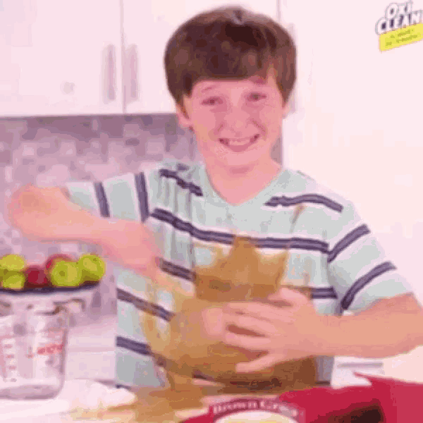 a young boy is making a mess in a kitchen while holding a bag of brownie mix .