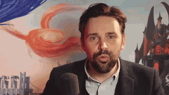 a man with a beard is talking into a microphone in front of a castle
