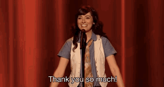 a woman stands in front of a red curtain and says thank you so much