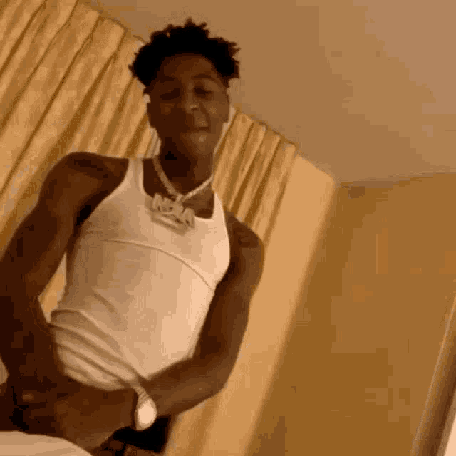 a young man in a white tank top is sitting on a bed in a room .