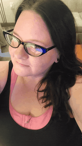 a woman wearing glasses and a pink tank top is smiling