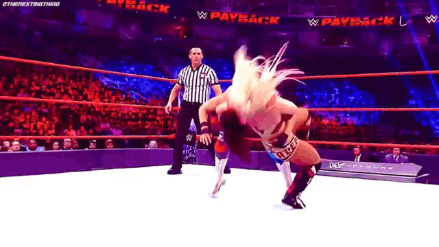 two women are wrestling in a wrestling ring with a referee watching .
