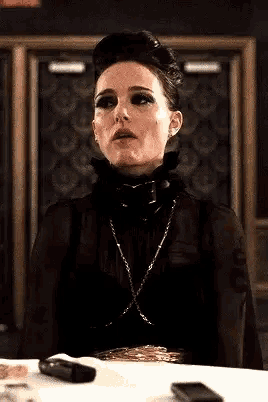 a woman is sitting at a table wearing a black dress and a chain around her neck .