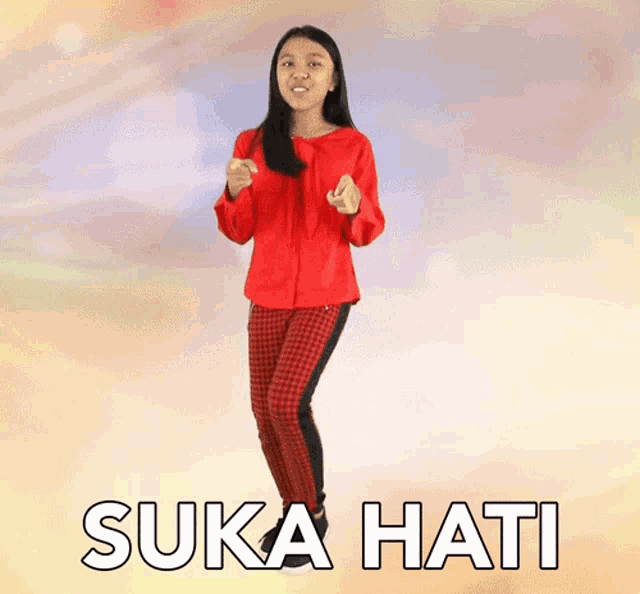 a girl in a red shirt and plaid pants is jumping in the air with the words suka hati below her