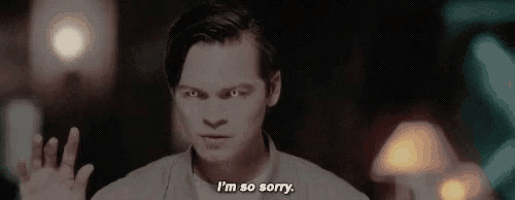 a man is waving his hand and saying `` i 'm so sorry '' while standing in a dark room .