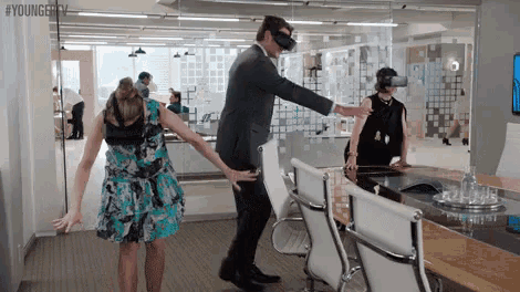 a man wearing a virtual reality headset is standing next to a woman in a blue dress .