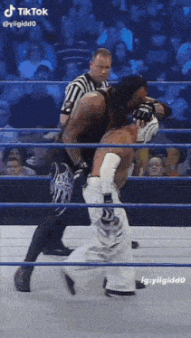 two wrestlers are fighting in a wrestling ring with a referee watching .