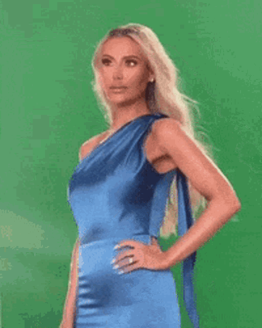 a woman in a blue one shoulder dress is standing in front of a green background .