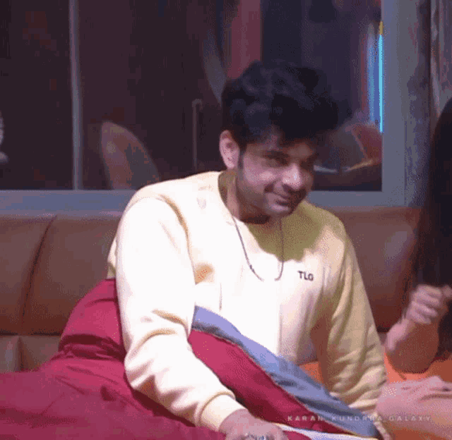 a man wearing a yellow tlg sweatshirt sits on a couch next to a woman