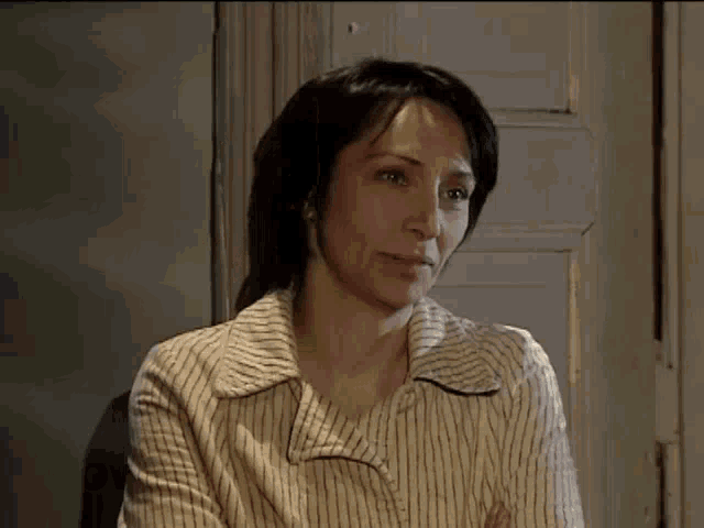 a woman in a striped shirt is sitting in front of a door with her arms crossed and looking at the camera .