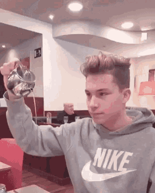 a young man wearing a nike sweatshirt is pouring liquid into a glass