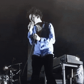 a man in a blue shirt is standing in front of a drum set on a stage