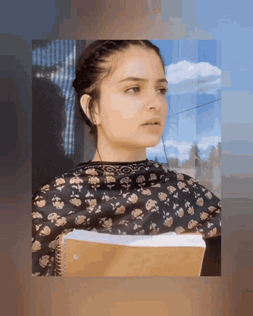 a woman in a black and gold floral top holds a notebook