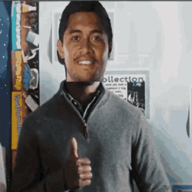 a man in a gray sweater is giving a thumbs up sign