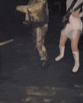 a woman in a white dress playing a guitar next to another woman in a camouflage jacket