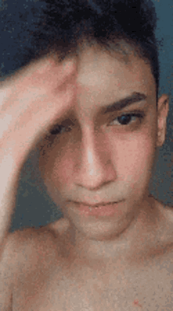 a young man without a shirt is touching his forehead .