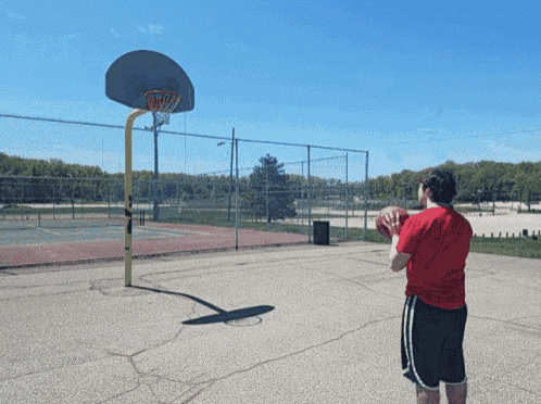 a man in a red shirt shoots a basketball