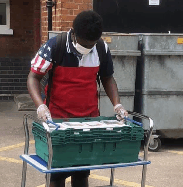 a man wearing a mask and gloves is pushing a cart with a green box on it .