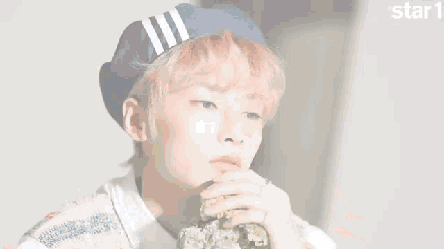 a young man with pink hair is wearing a purple beret and eating a piece of broccoli .