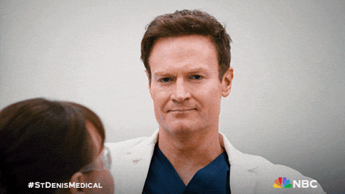 a man in a lab coat is talking to a woman with the nbc logo in the corner