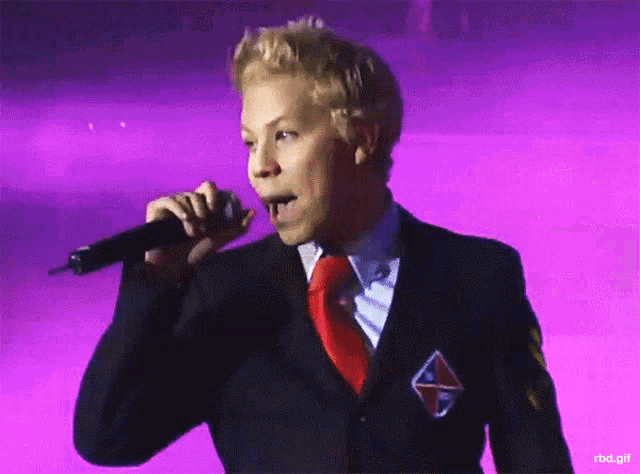 a man in a suit is singing into a microphone with a purple background