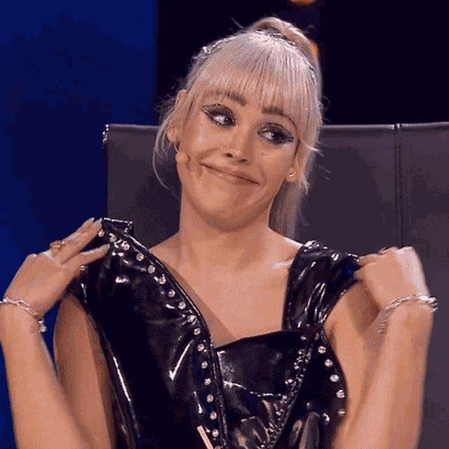 a woman with blonde hair is wearing a black leather dress and making a funny face