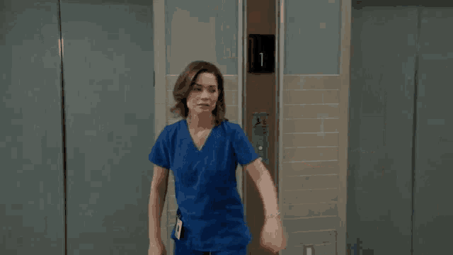 a woman in a blue scrub top is standing next to a man in a black shirt in front of an elevator .