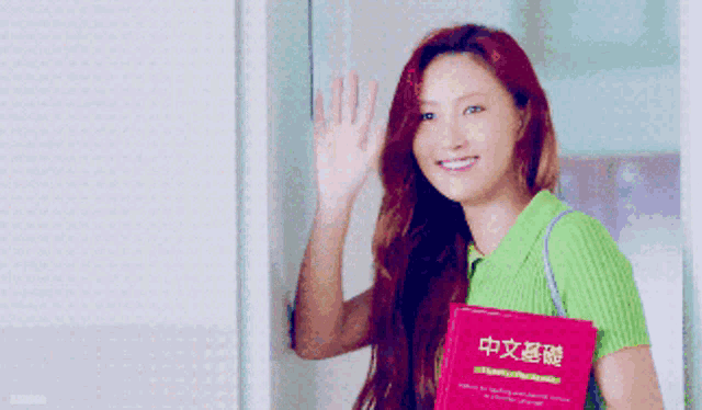 a woman in a green shirt is holding a pink book with chinese characters on it