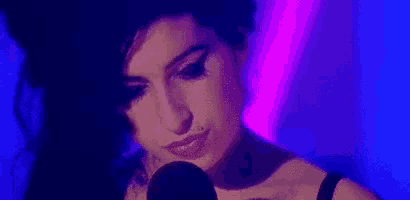 a woman is singing into a microphone in a dark room with purple lights behind her .