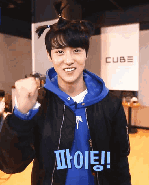 a boy wearing a blue hoodie and a black jacket with the word cube behind him