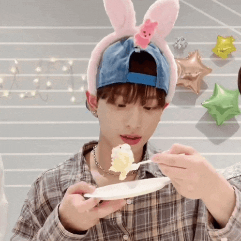 a young boy wearing a bunny ear headband is eating a piece of cake with a spoon .