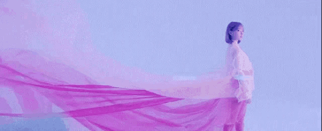 a woman in a white dress is standing in front of a purple cloth that is blowing in the wind