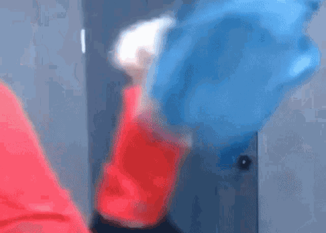 a man in a red shirt is standing in front of a door holding a blue bag .