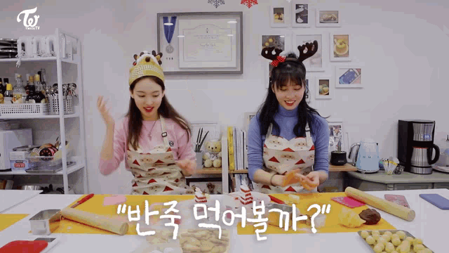 two women wearing aprons and reindeer antlers sit at a table with korean writing on it